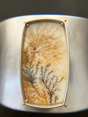 Silver cuff bracelet with a dendritic agate stone inlay on a gray surface