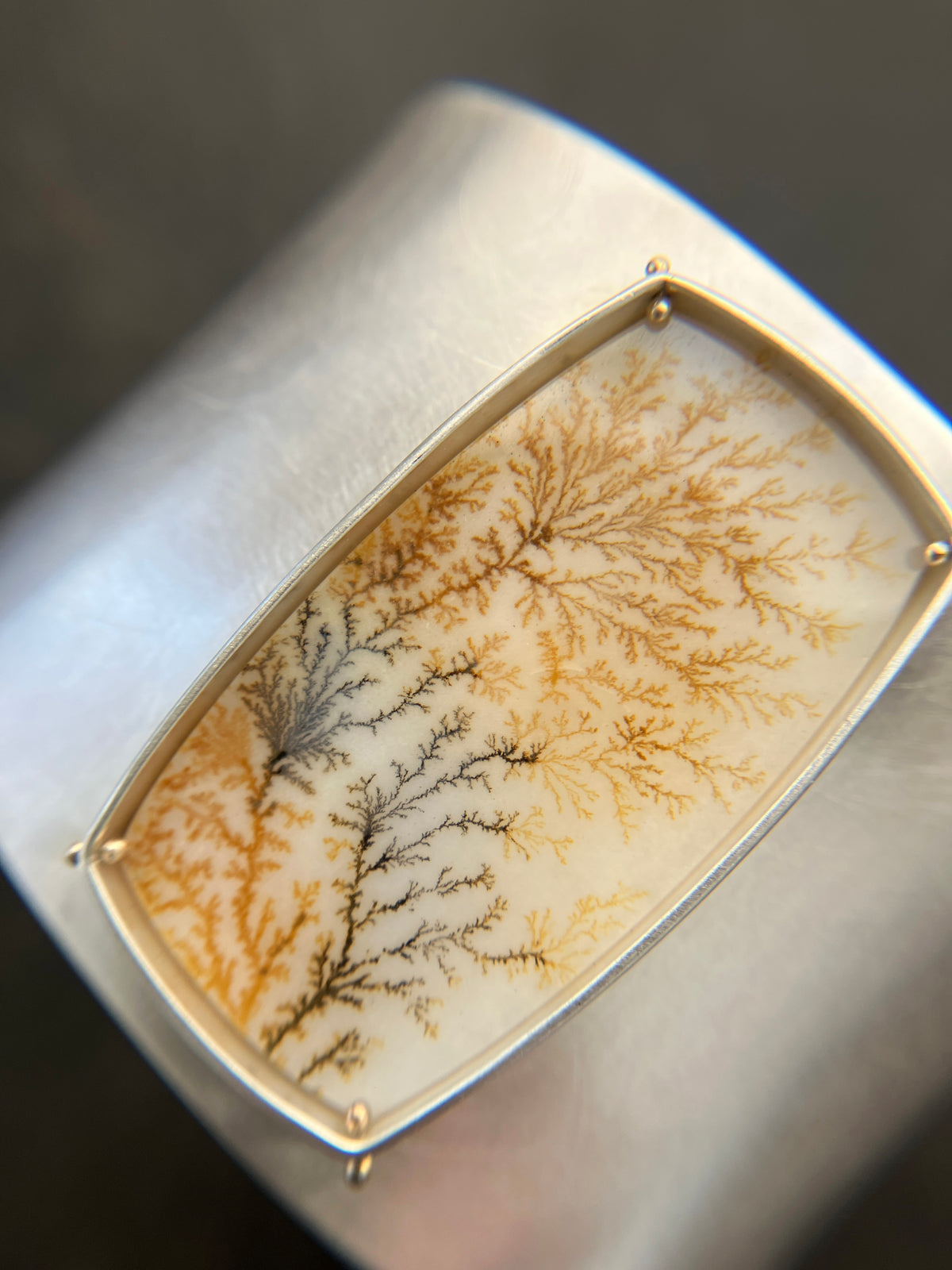 Silver cuff bracelet with a dendritic agate stone inlay on a gray surface