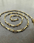 A gold elongated oval chain necklace coiled in a spiral on a textured gray surface.