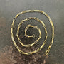 A gold elongated oval chain necklace coiled in a spiral on a textured gray surface.