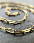 A gold elongated oval chain necklace coiled in a spiral on a textured gray surface.
