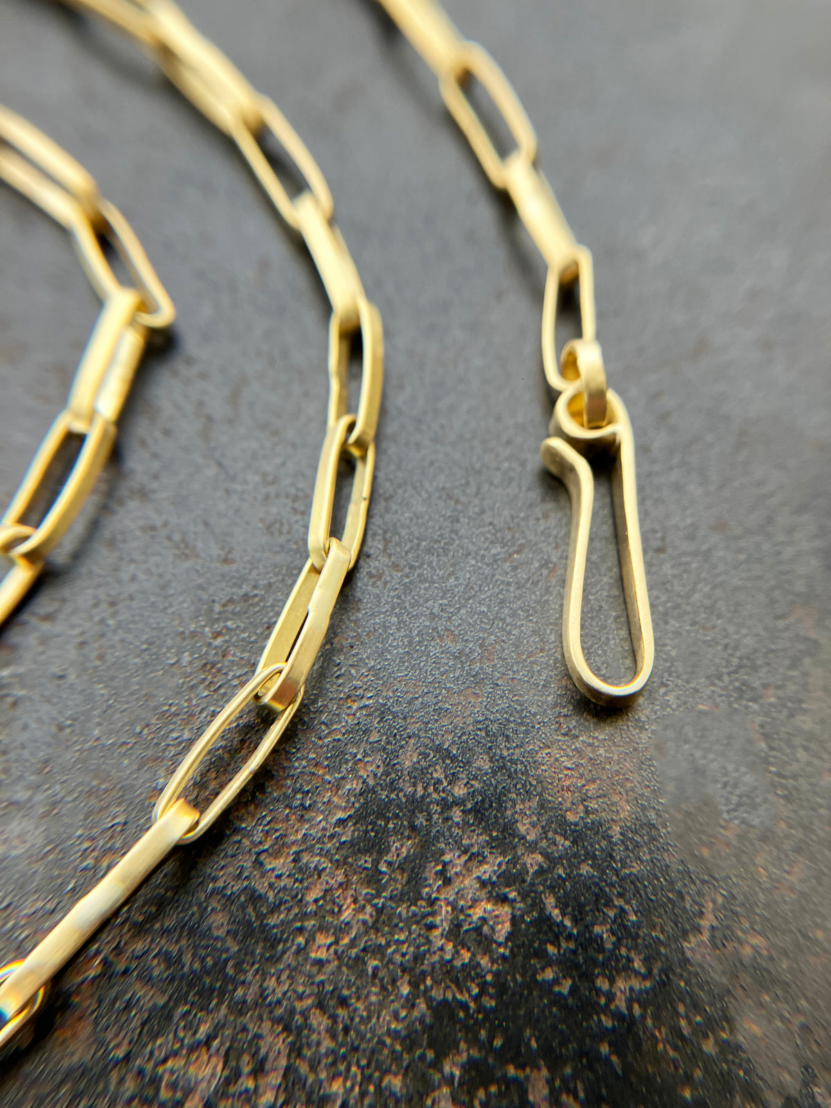 An 18k gold elongated oval chain necklace coiled in a spiral on a textured gray surface.