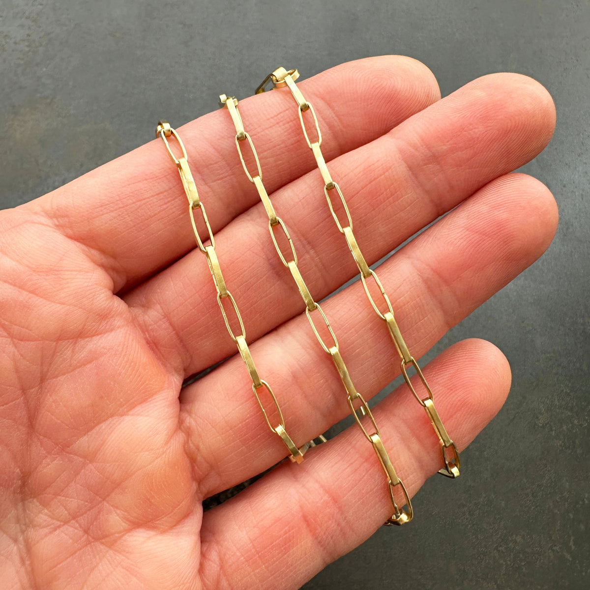 An 18k gold elongated oval chain necklace coiled in a spiral on a hand.