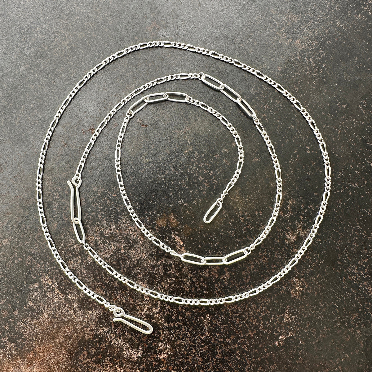 Silver  figaro chain necklace on a textured dark surface
