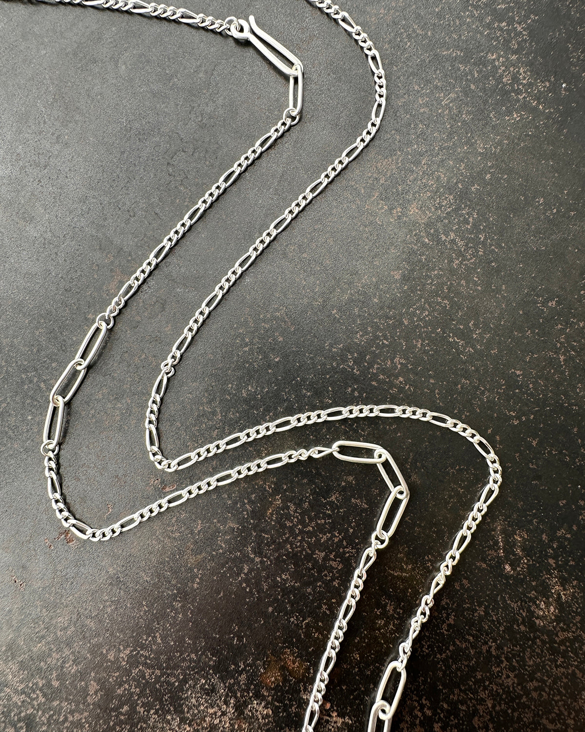 Silver  figaro chain necklace on a textured dark surface