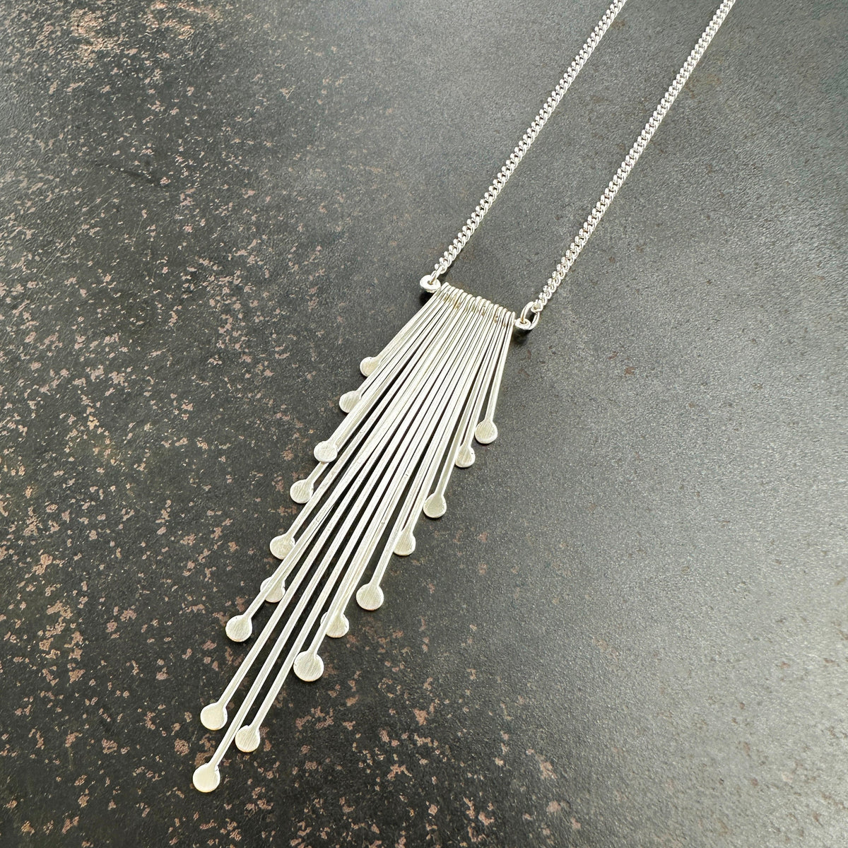 Silver necklace with a fan-shaped pendant on a dark surface