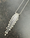 Silver necklace with a fan-shaped pendant on a dark surface