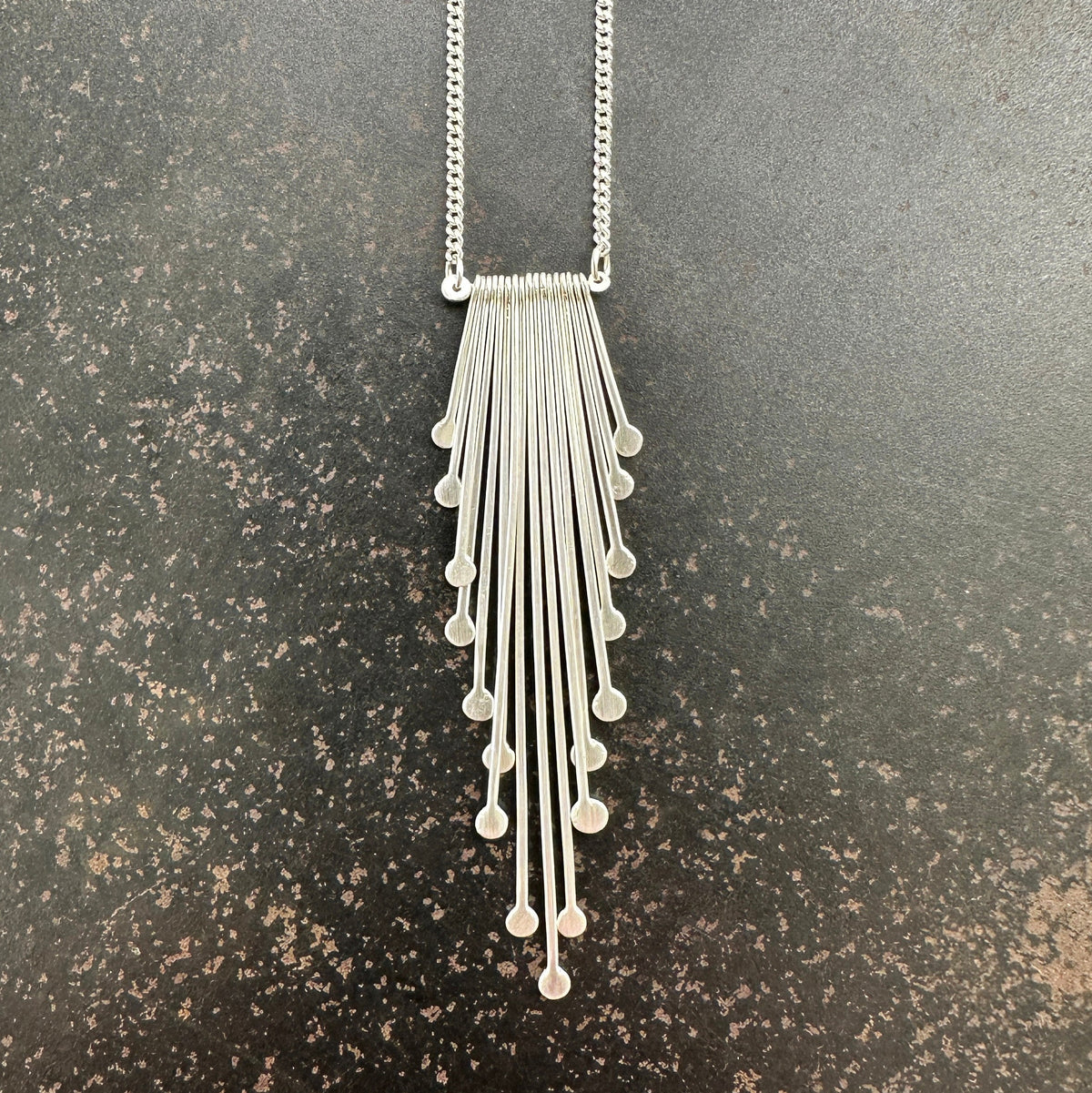 Silver necklace with dangling fringe on a gray surface
