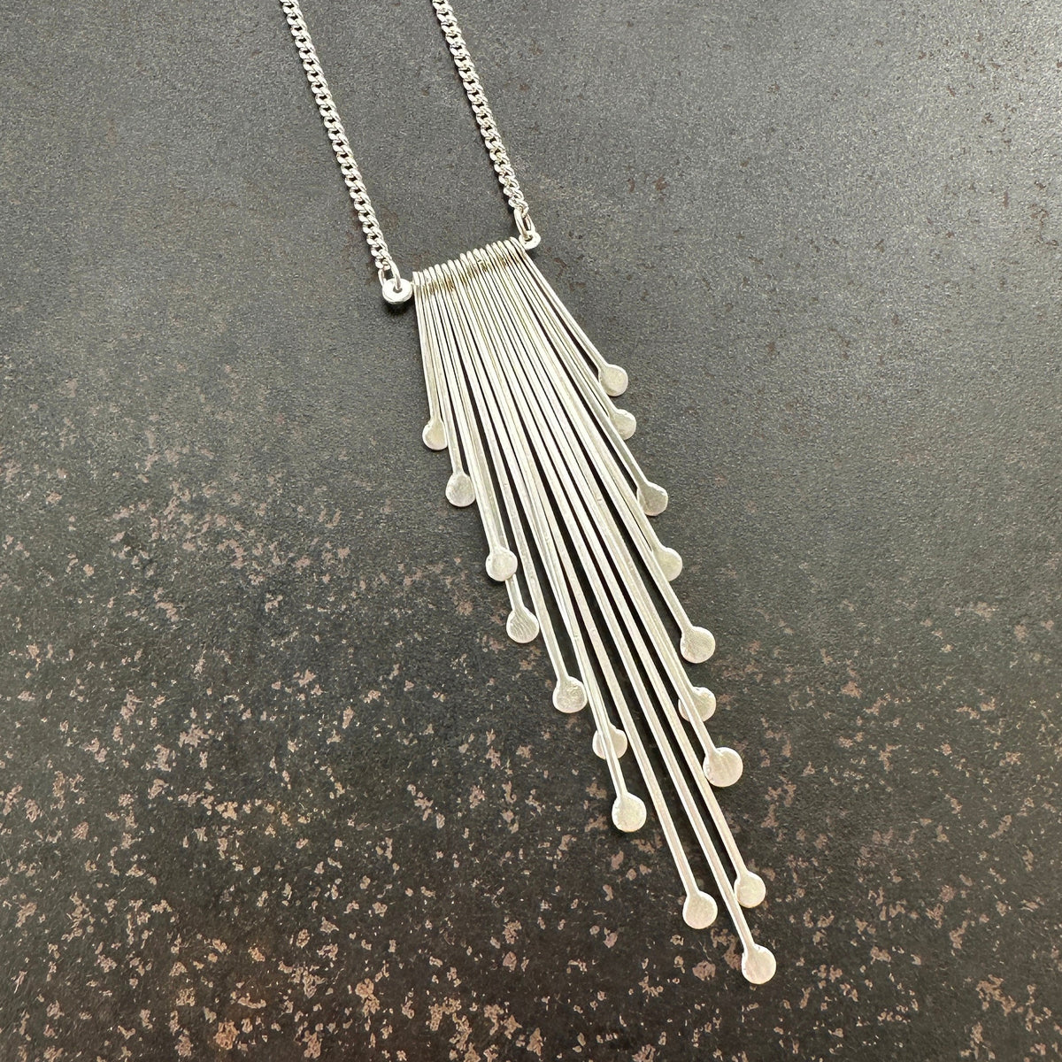 Silver fringe necklace on a dark textured surface