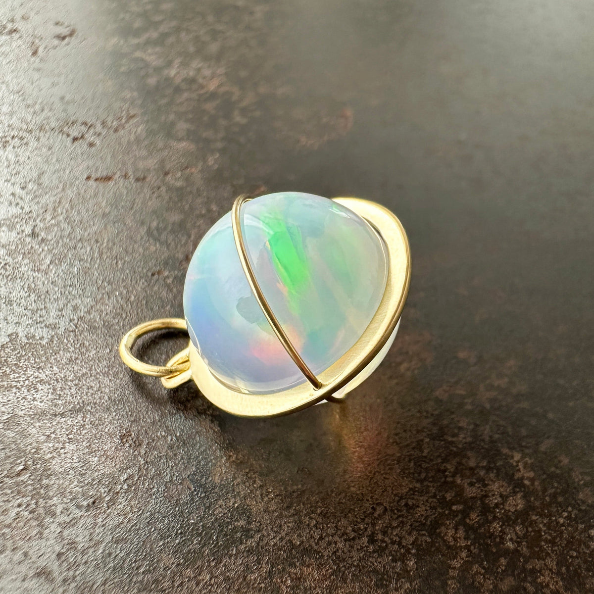 Opal orb pendant in a gold setting on a dark surface