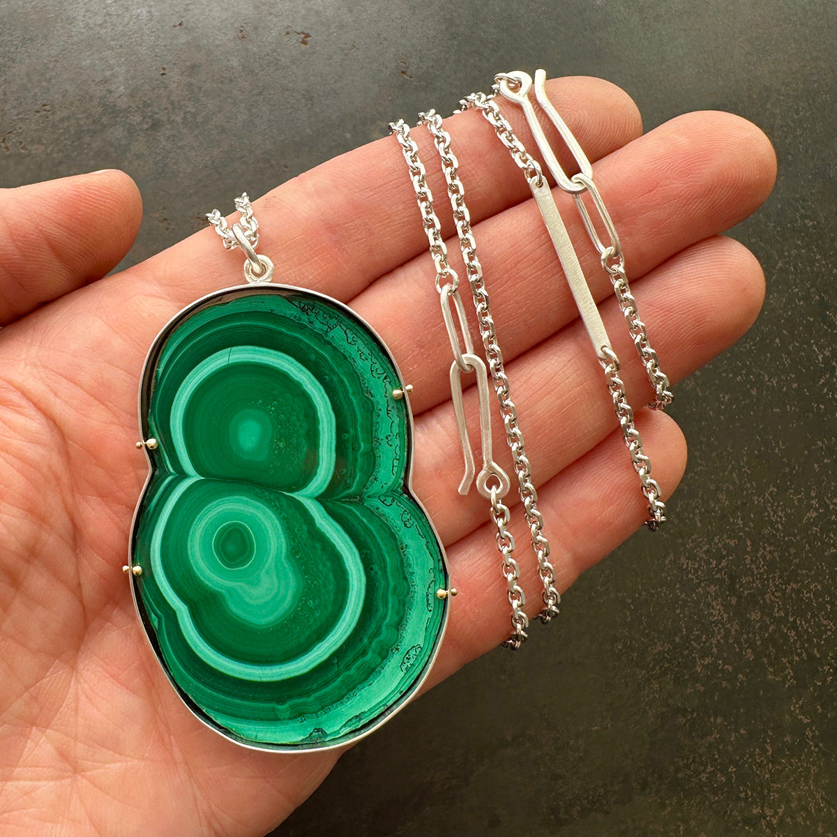 Green malachite pendant on a silver chain held in a hand against a dark background