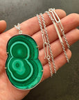 Green malachite pendant on a silver chain held in a hand against a dark background