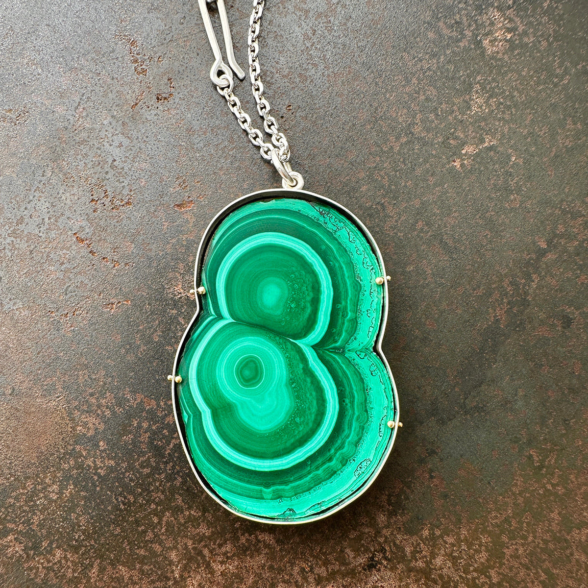Green malachite pendant on a silver chain against a textured brown background