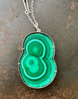 Green malachite pendant on a silver chain against a textured brown background