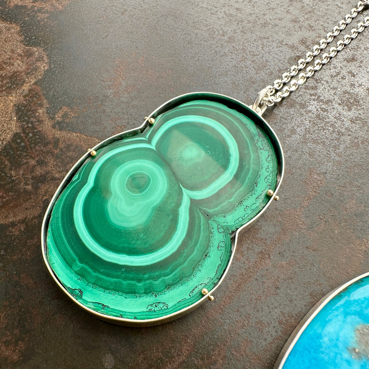 Green malachite pendant on a chain against a textured brown background