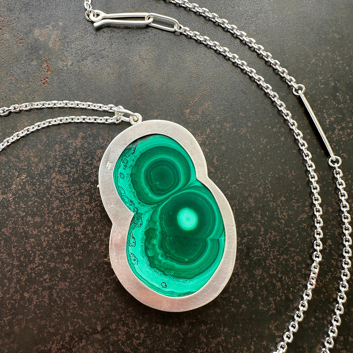 Necklace with a green malachite and silver pendant on a dark surface