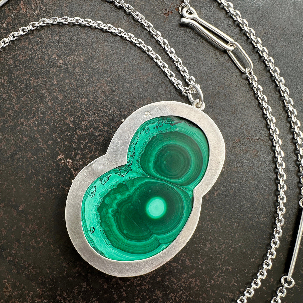 Necklace with a green malachite and silver pendant on a dark surface