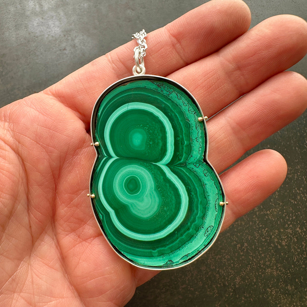 Green malachite pendant held in a hand against a dark background