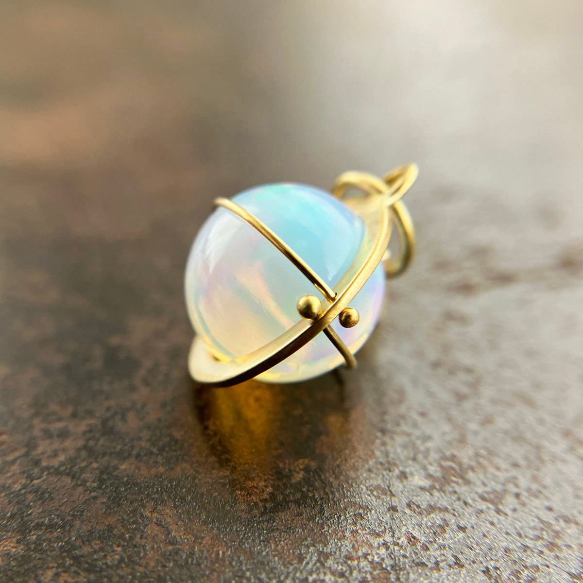 An ethiopian opal orb pendant in an 18k gold setting