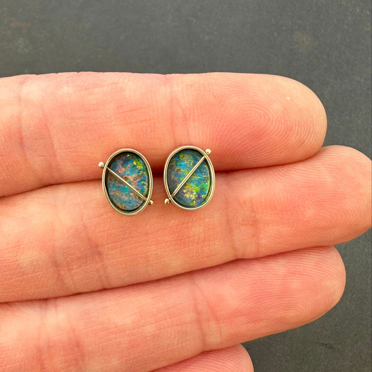 Pair of opal stud earrings held between fingers against a dark background