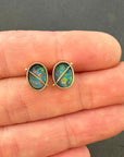 Pair of opal stud earrings held between fingers against a dark background