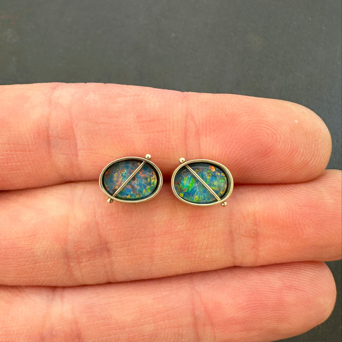 Opal stud earrings held between two fingers against a dark background