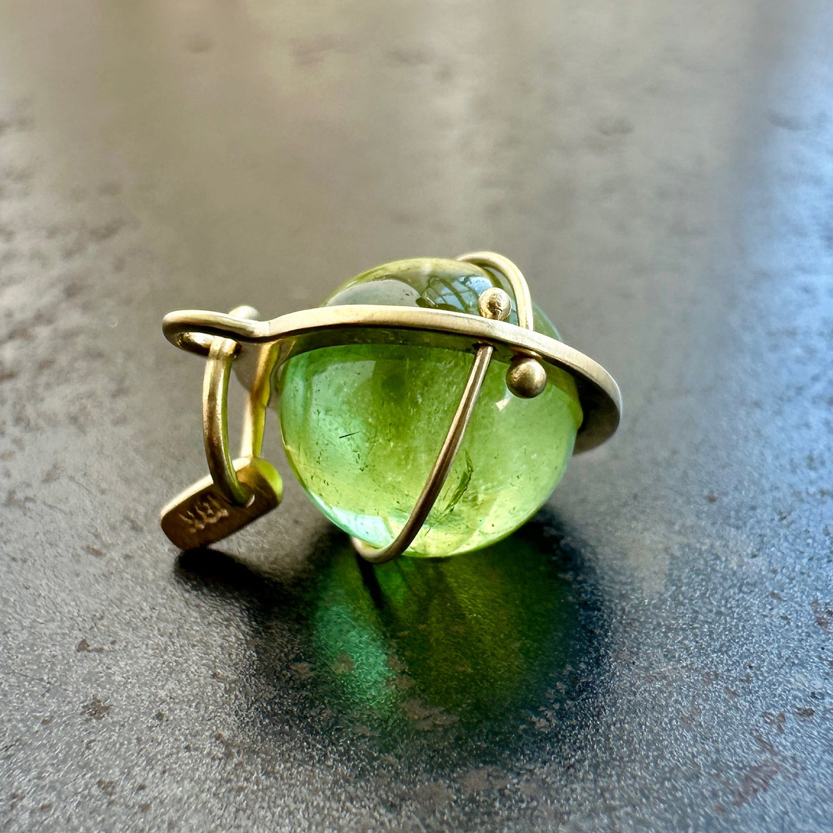 An 18k gold orb pendant with a green peridot sphere gemstone.
