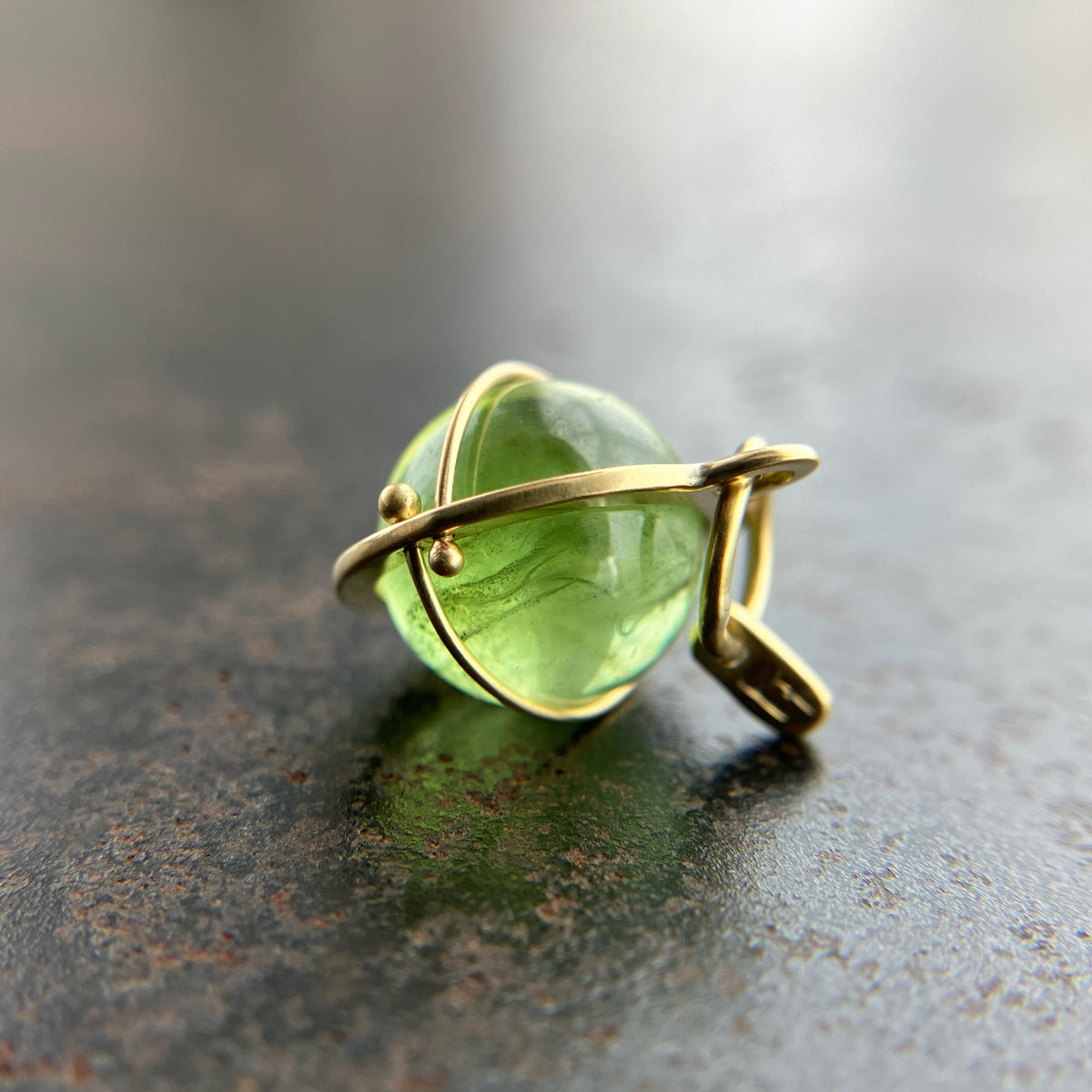 An 18k gold orb pendant with a green peridot sphere gemstone.