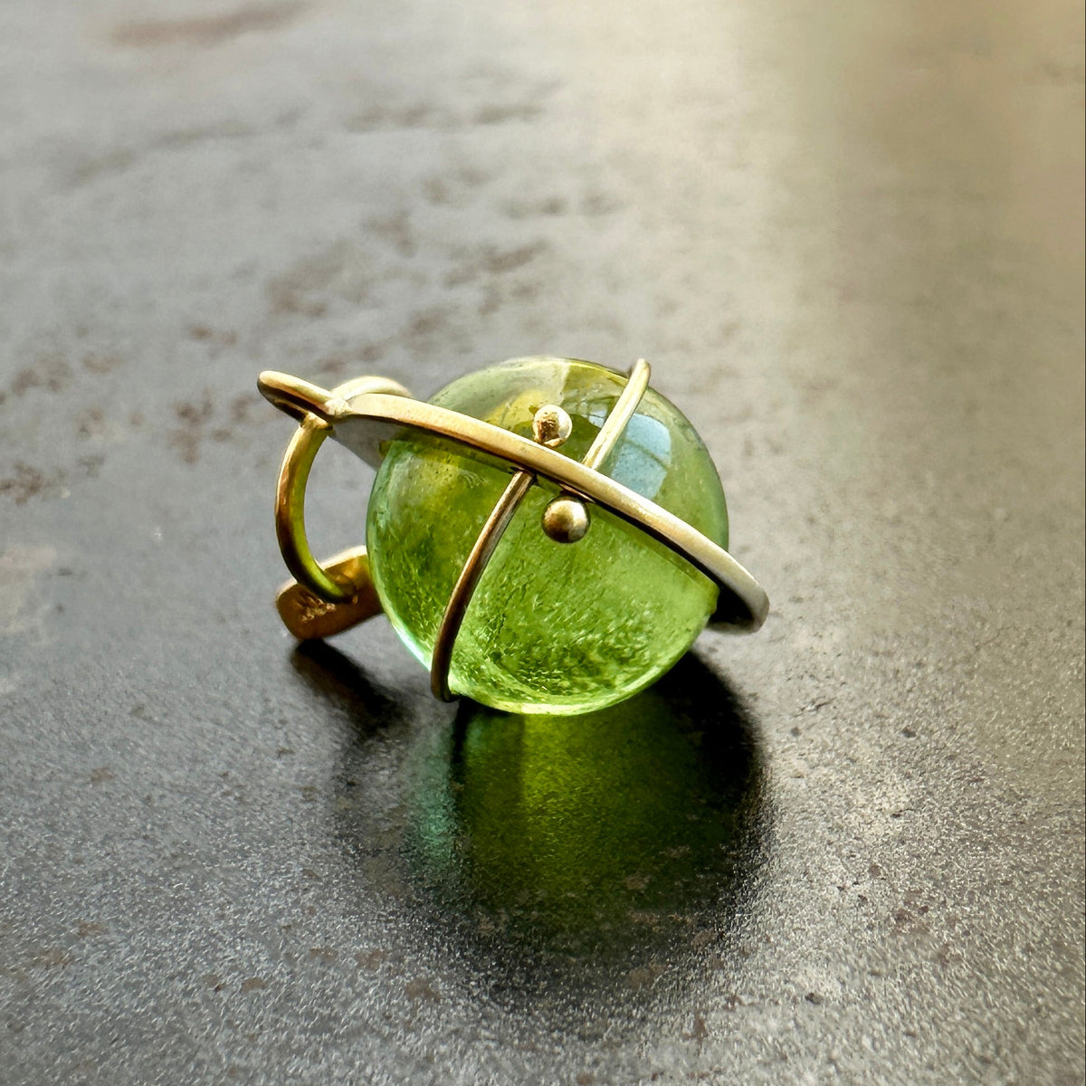 An 18k gold orb pendant with a green peridot sphere gemstone.