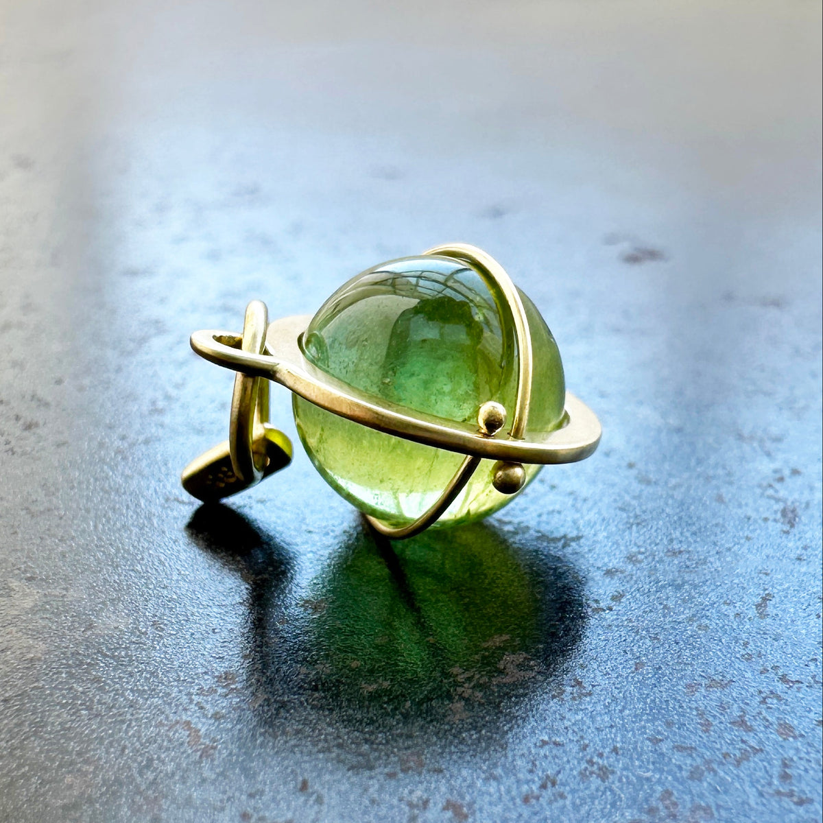 An 18k gold orb pendant with a green peridot sphere gemstone.