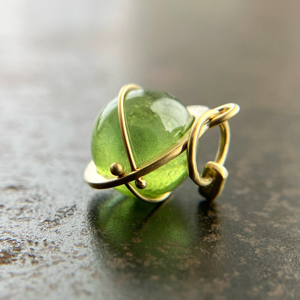 An 18k gold orb pendant with a green peridot sphere gemstone.