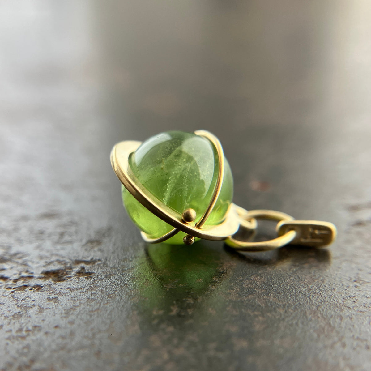 An 18k gold orb pendant with a green peridot sphere gemstone.