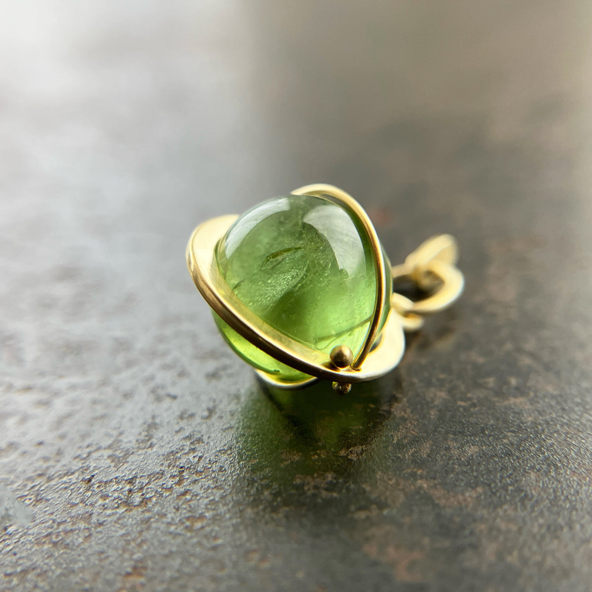 An 18k gold orb pendant with a green peridot sphere gemstone.