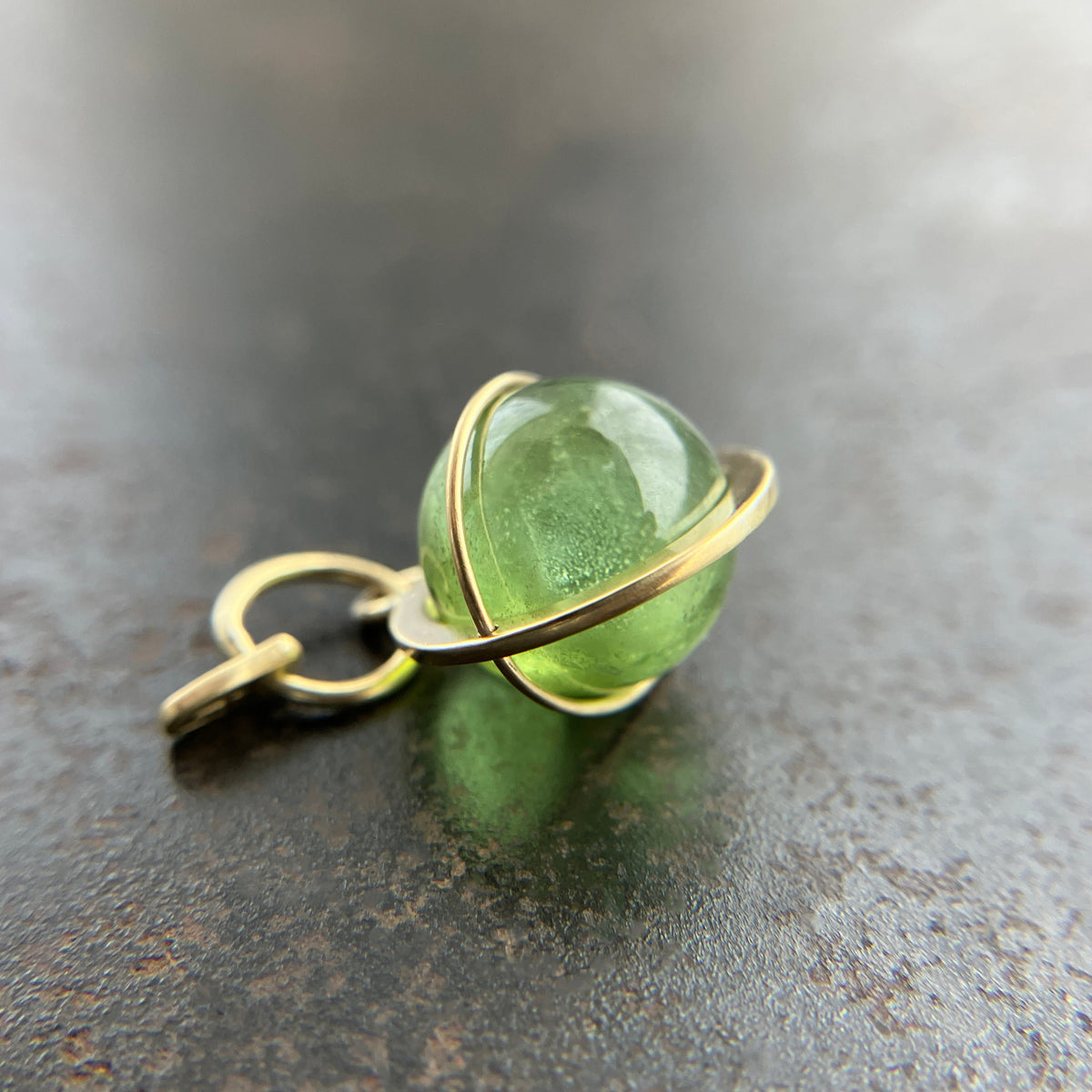 An 18k gold orb pendant with a green peridot sphere gemstone.