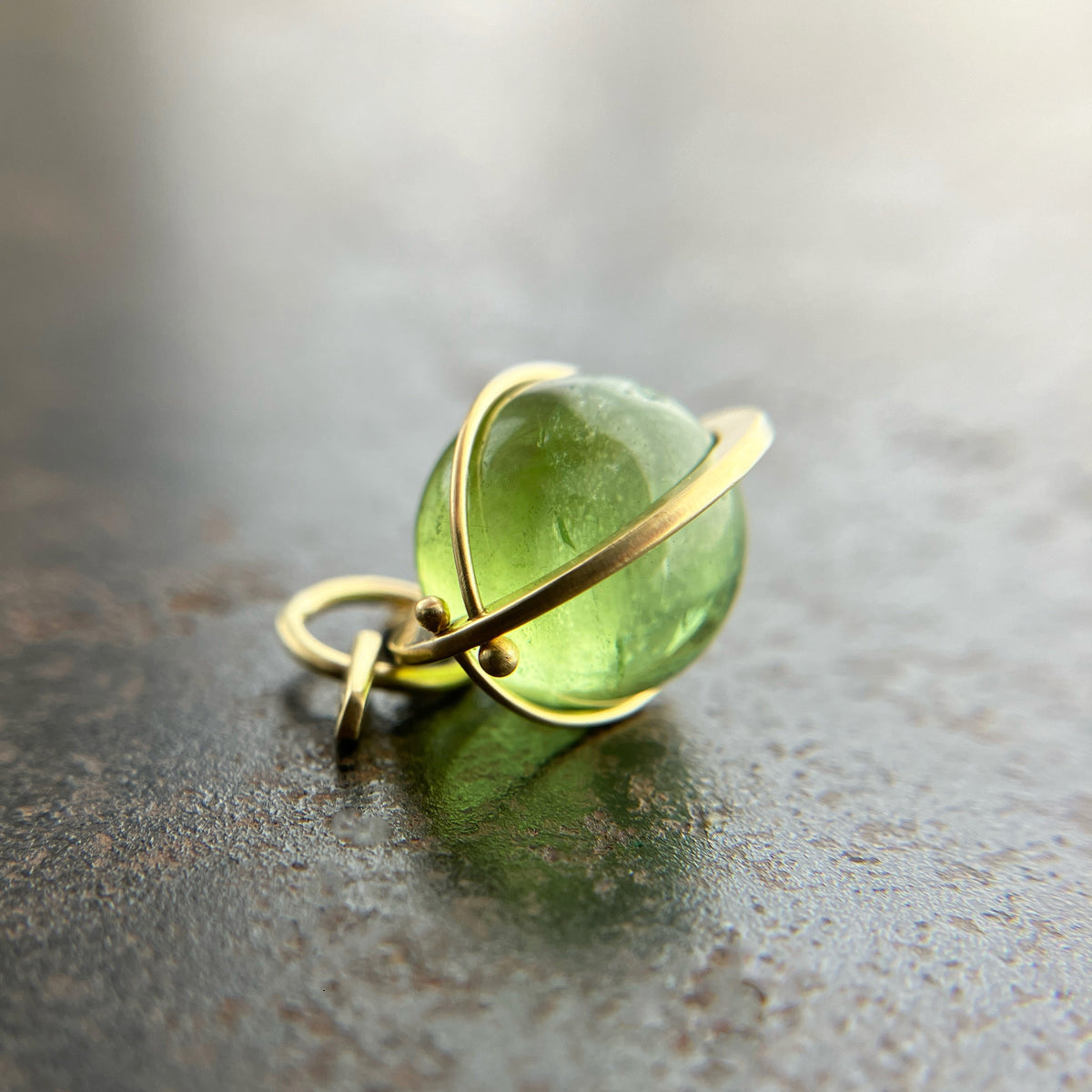 An 18k gold orb pendant with a green peridot sphere gemstone.