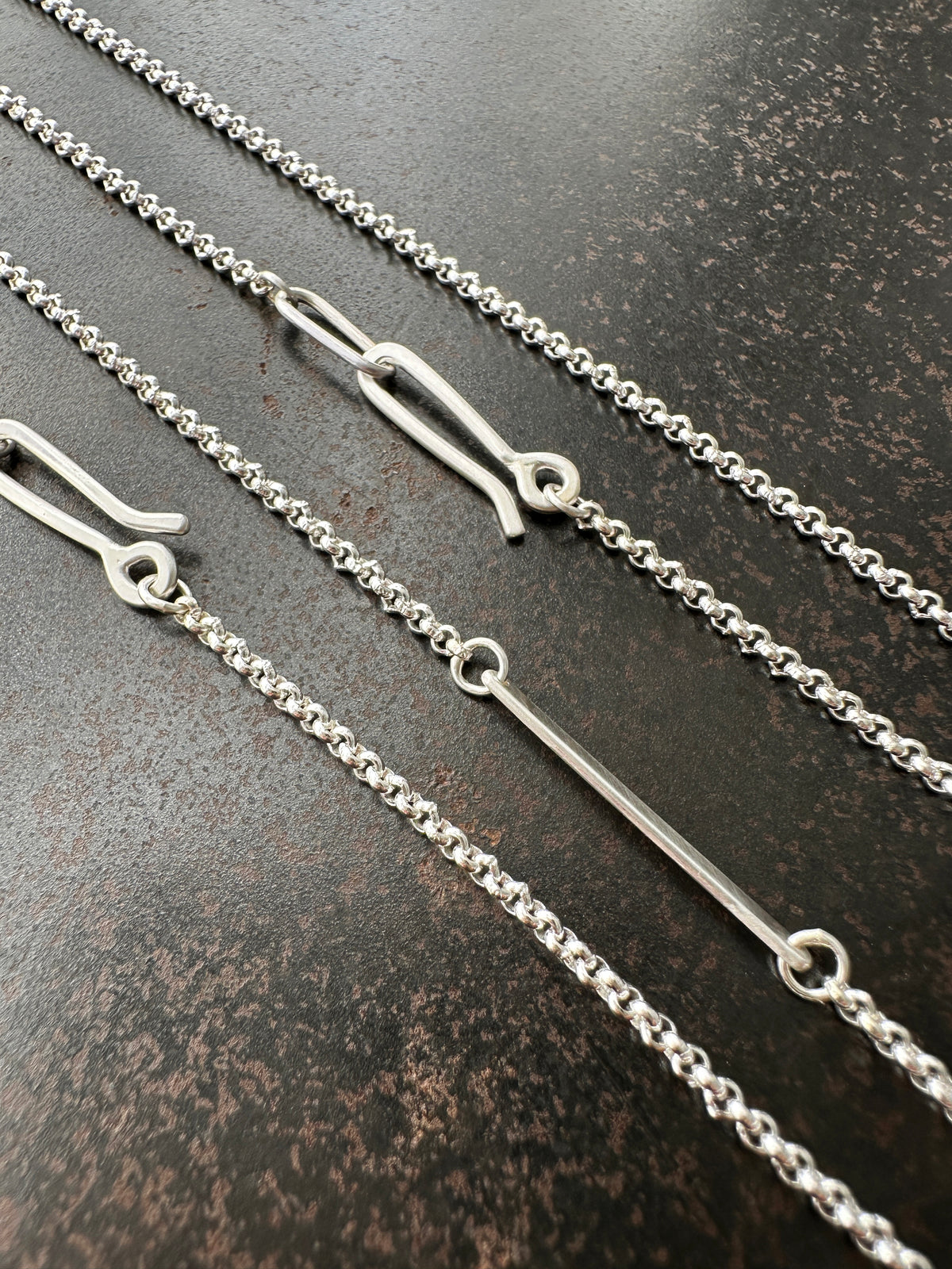 Silver rolo chain necklace on a dark textured surface