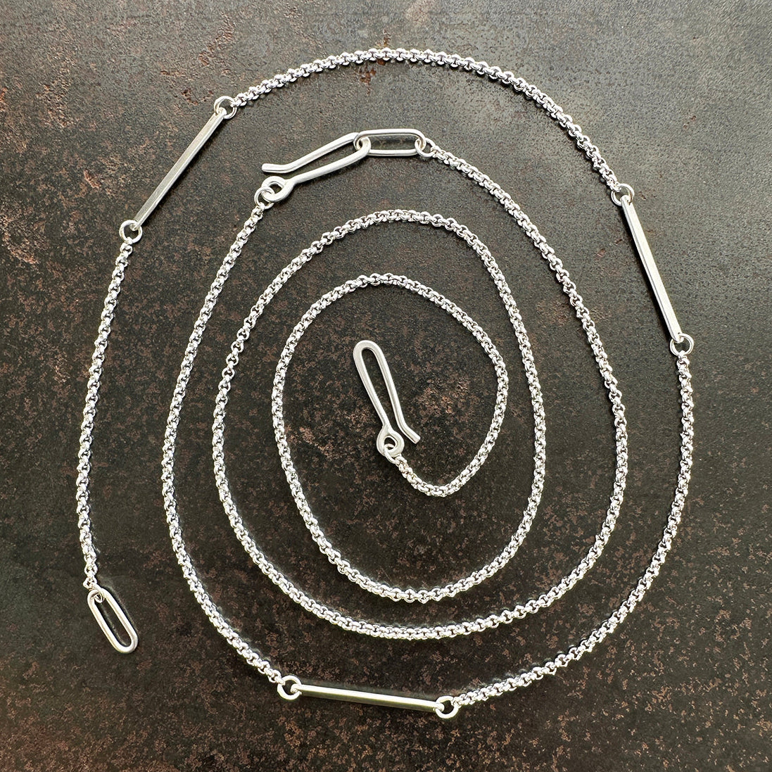 Silver rolo chain necklace on a dark textured surface