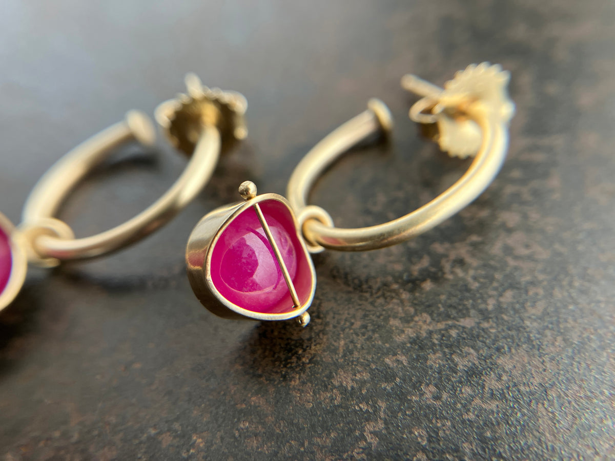 14k Gold hoop earrings with a bright pink ruby gemstone hoop charm, shown close up on a dark textured surface.