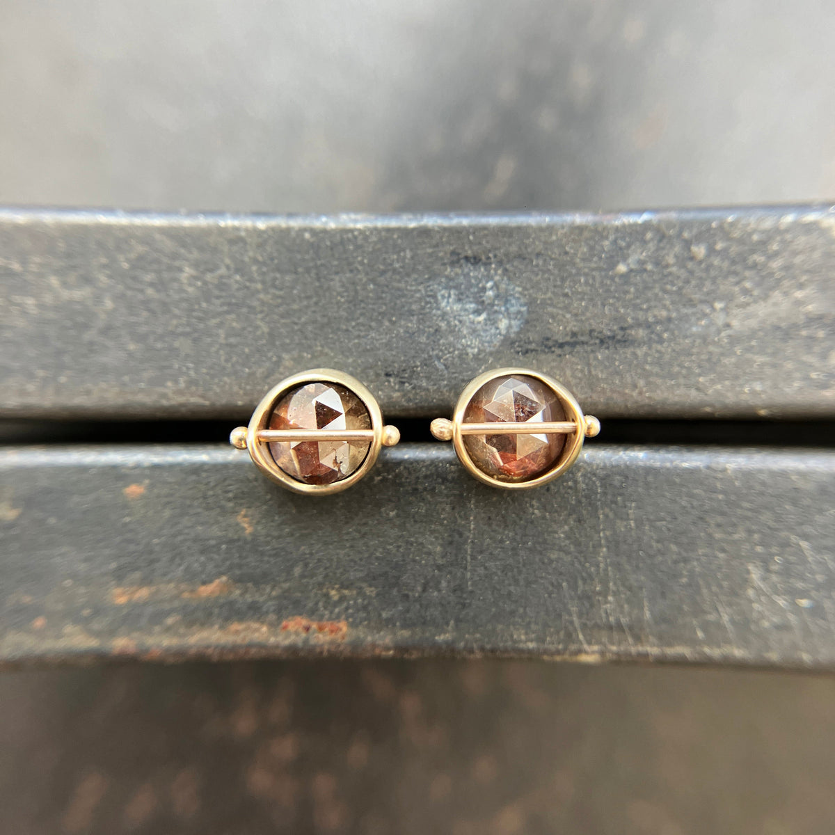 Pair of gold stud earrings with rustic diamond on a dark surface