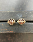 Pair of gold stud earrings with rustic diamond on a dark surface