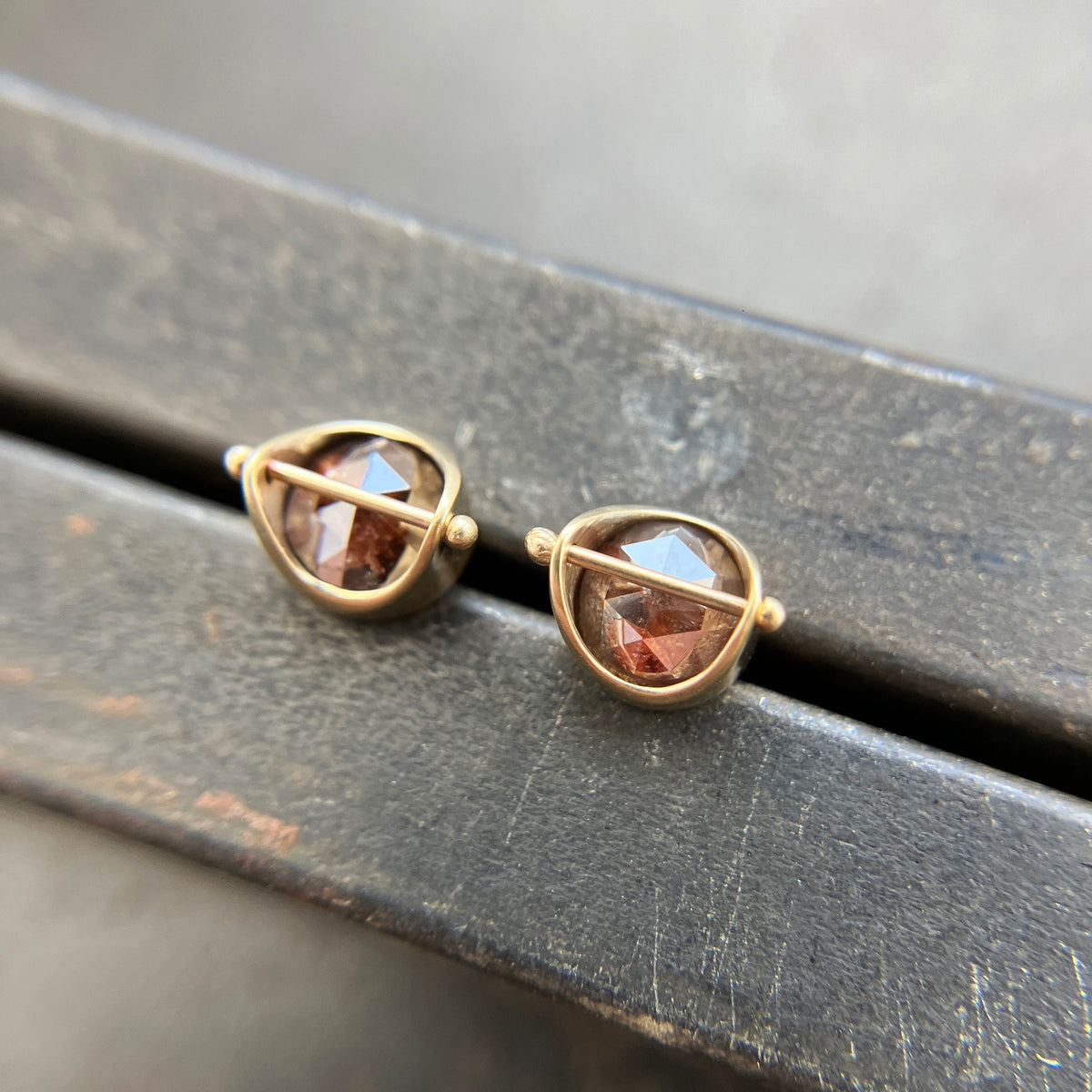 Pair of gold stud earrings with rustic diamond on a dark surface