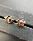 Pair of gold stud earrings with rustic diamond on a dark surface
