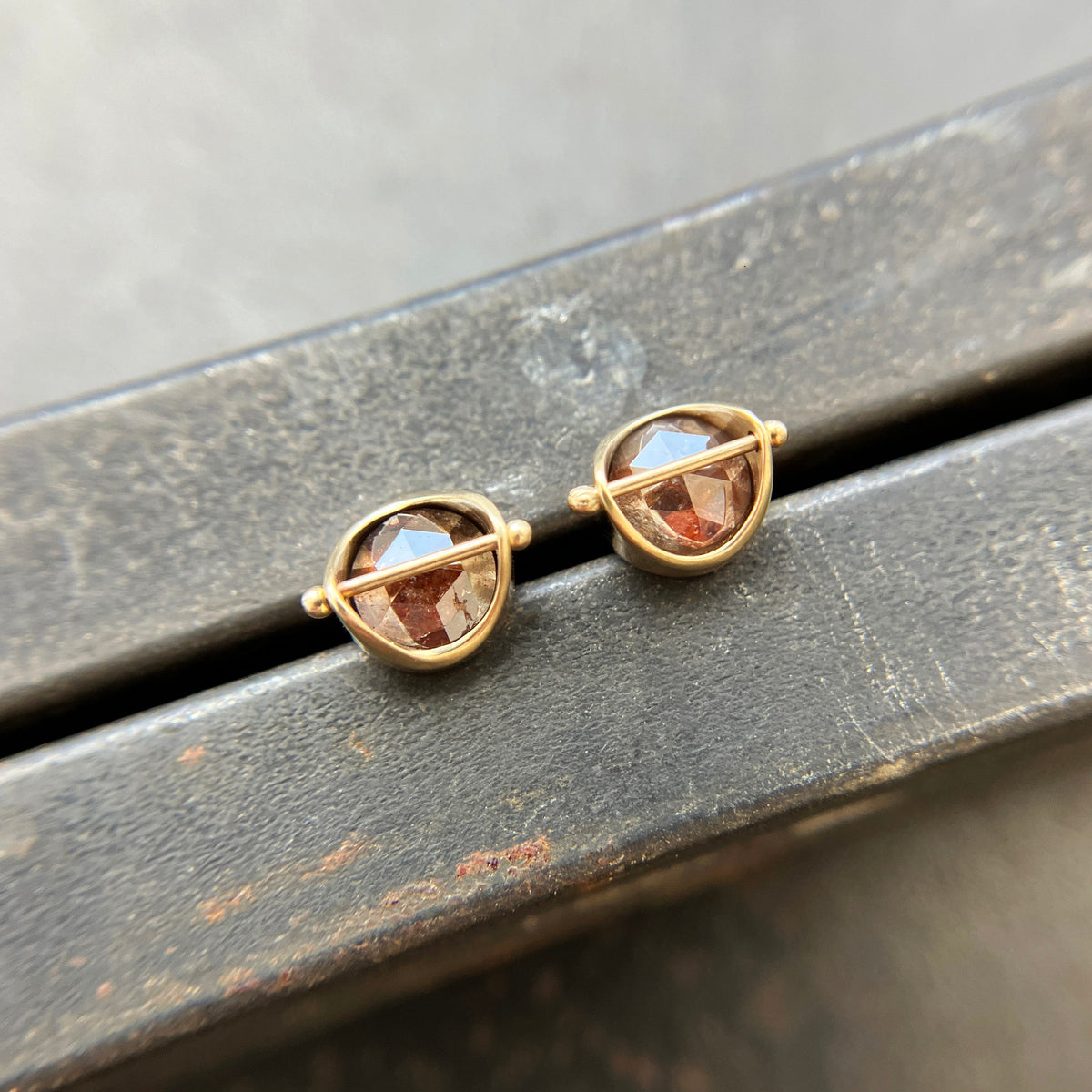 Pair of gold stud earrings with rustic diamond on a dark surface