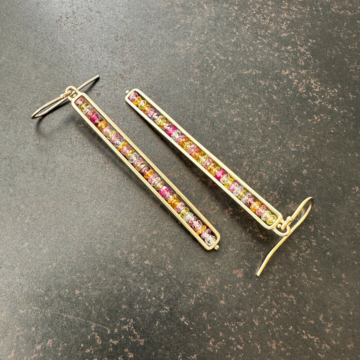 14k Gold bar earrings with colorful sapphire gemstones on a dark surface