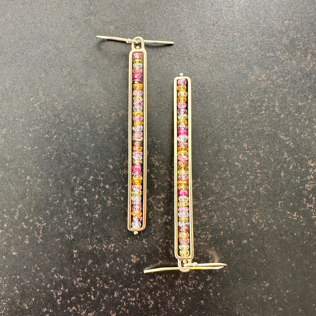 14k Gold bar earrings with colorful sapphire gemstones on a dark surface