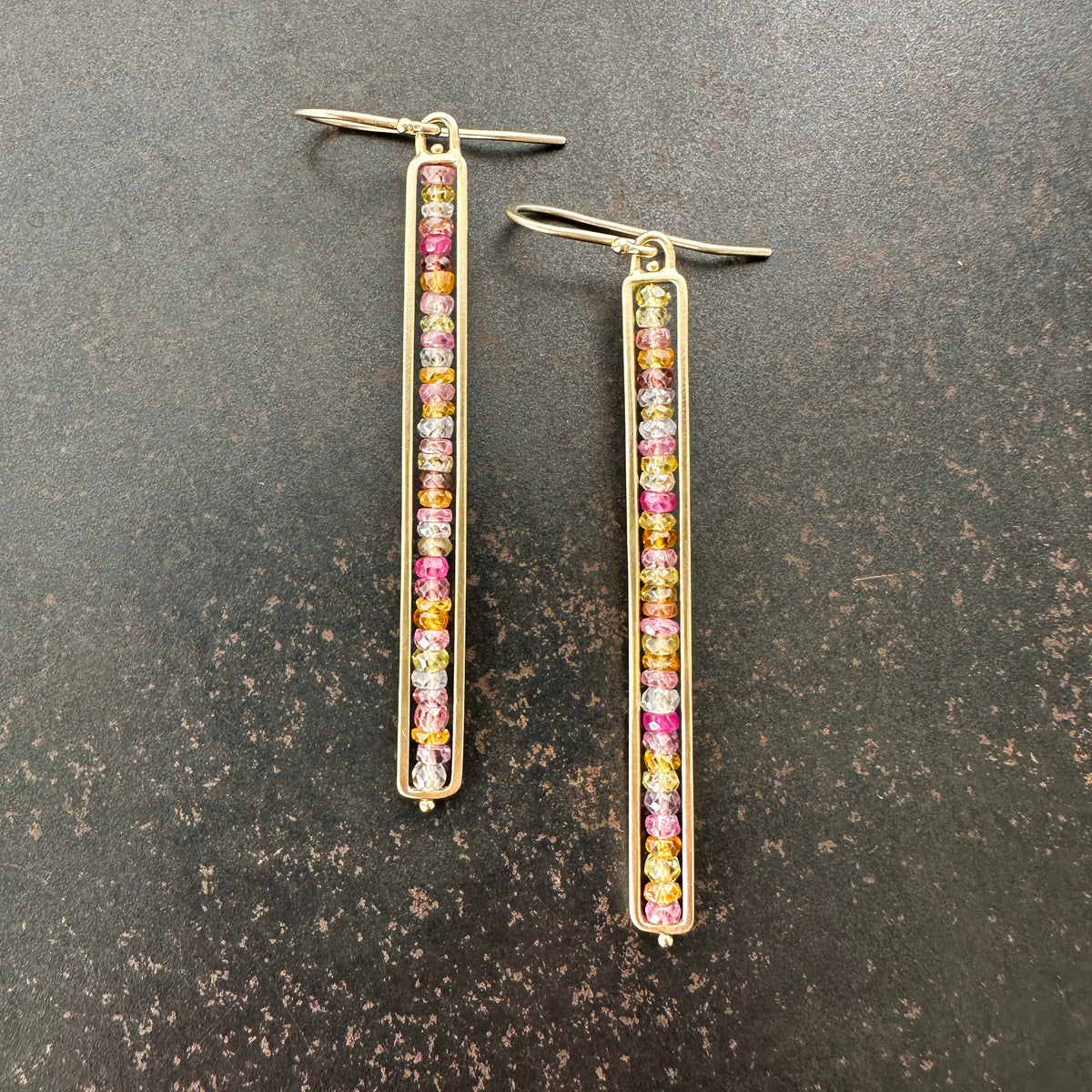 14k Gold bar earrings with colorful sapphire gemstones on a dark surface