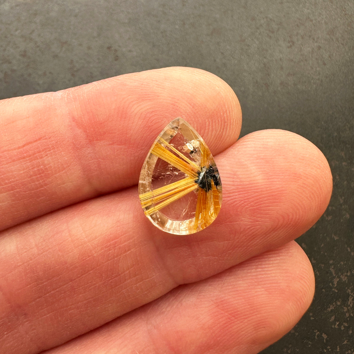 A teardrop-shaped gemstone featuring a striking golden-yellow radial pattern with a small dark inclusions, centered on a hand.