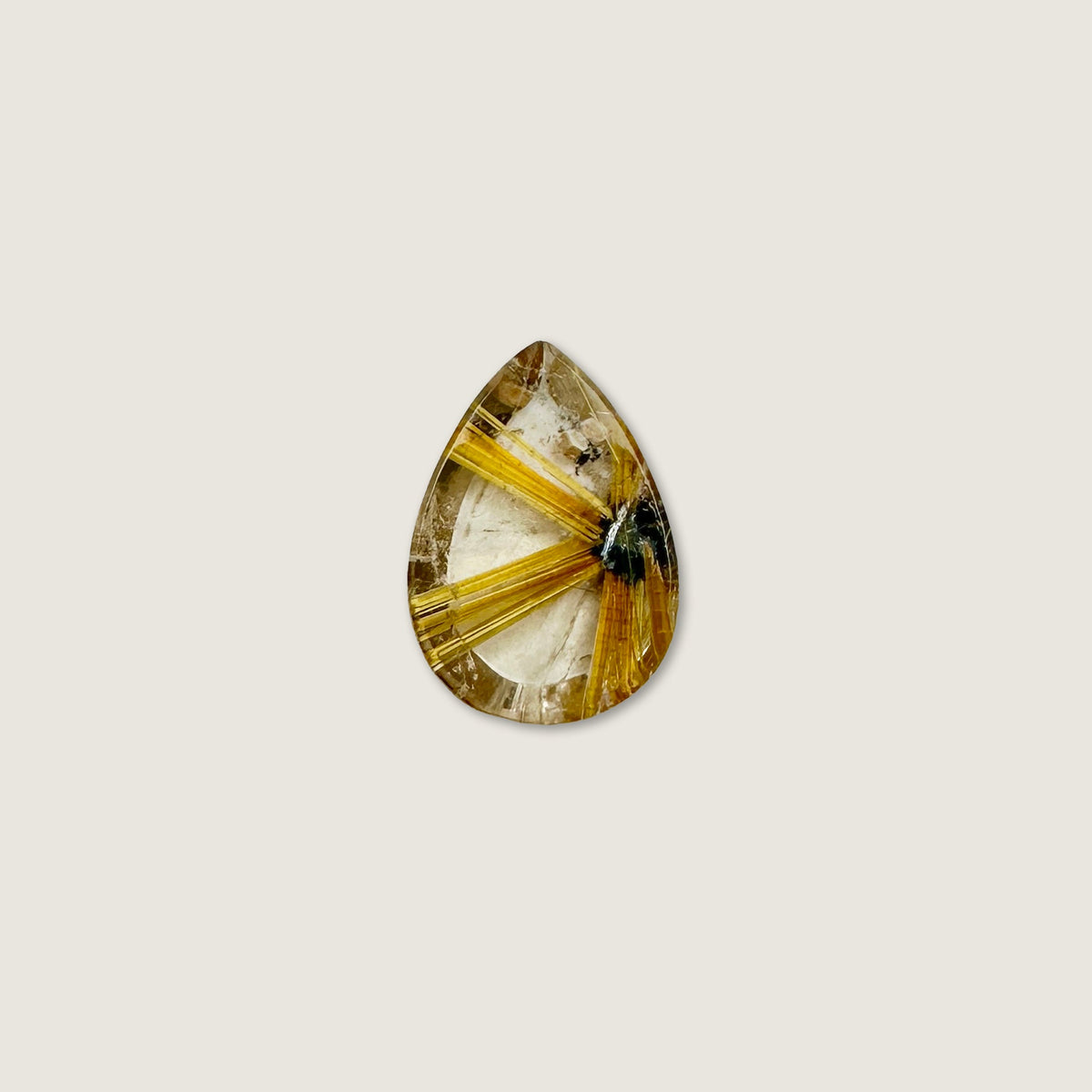 A teardrop-shaped gemstone featuring a striking golden-yellow and cream radial pattern with a small dark inclusions, centered on a solid light beige background.