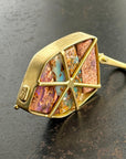 An 18k gold geometric pendant with wood replacement opals in shades of pink, blue, and purple, displayed on a dark textured surface.