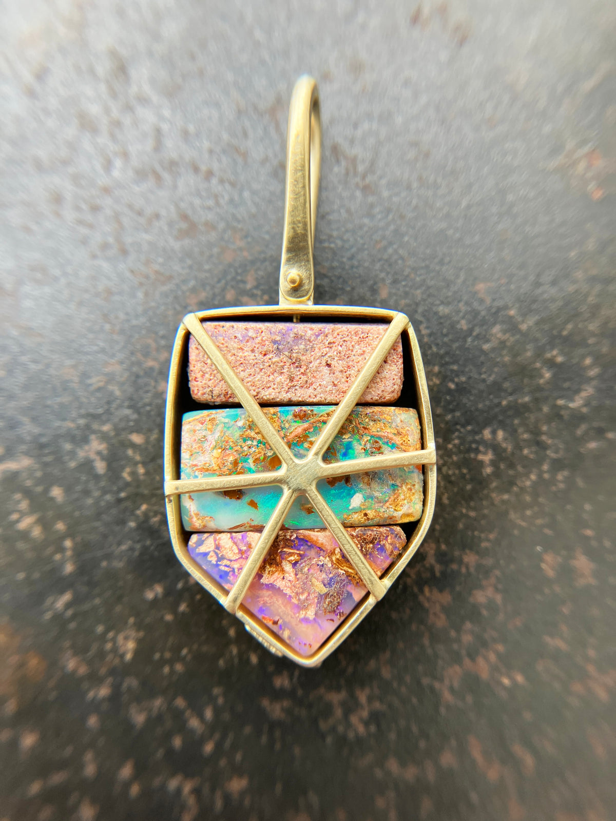 A shield-shaped pendant featuring an 18k gold frame and three rectangular inlay wood replacement opals in pink, turquoise, purple, and brown.